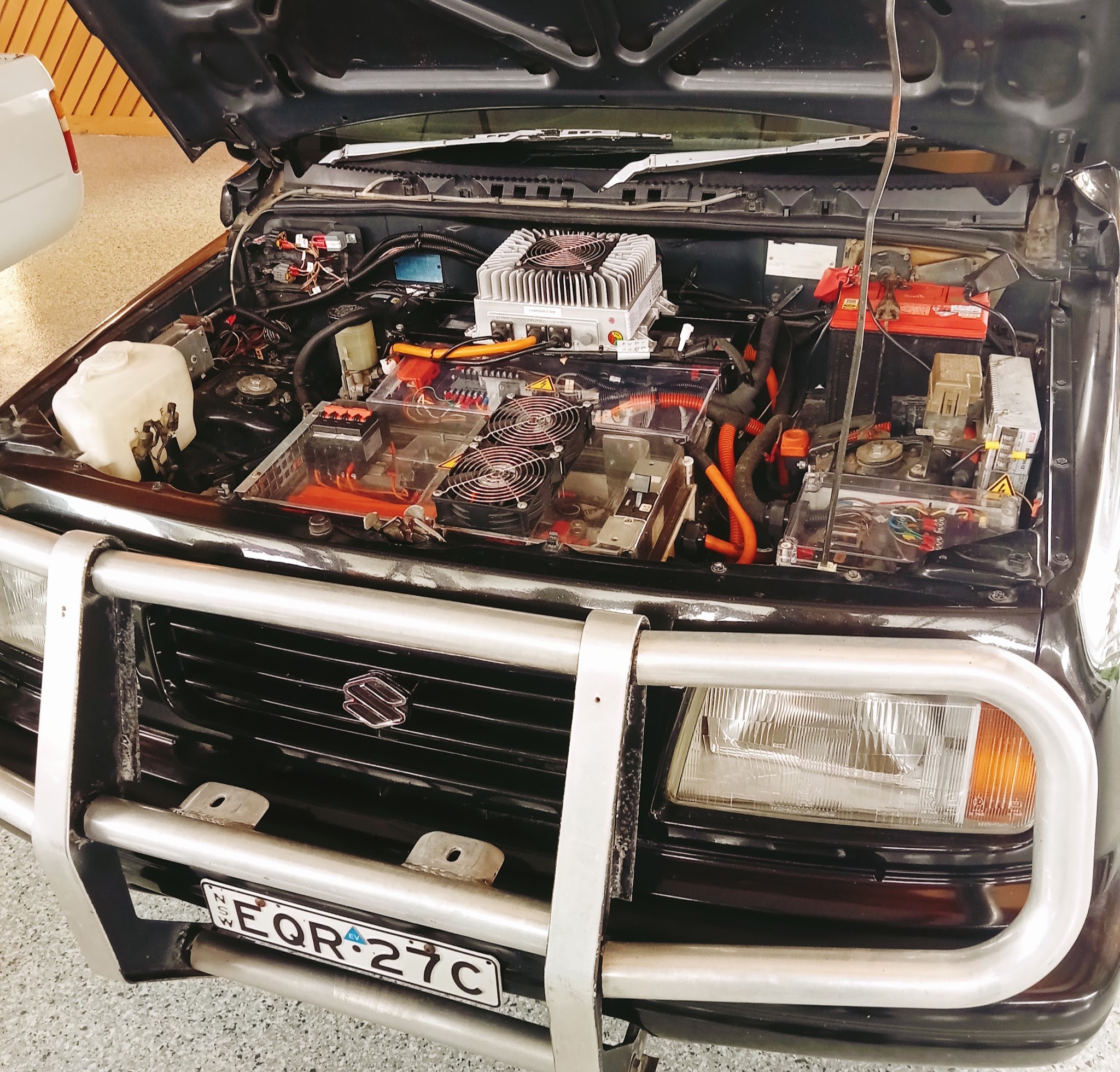 A four wheel drive in the workshop with its bonnet up over an electric drive conversion, showing the controller, converter and high voltage cabling